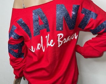 May include: Red off-the-shoulder sweatshirt with navy blue glitter lettering that says "Atlanta" and "Home of the Braves" in white lettering.
