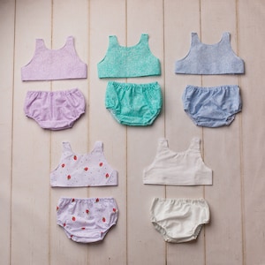May include: Set of six doll-sized underwear sets, each with a different patterned top and bottom. The tops are sleeveless and the bottoms are bloomers. The patterns include floral, polka dot, and solid colors.