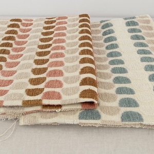 May include: Two rolls of patterned fabric. One has rows of half-circle shapes in brown, pink, and beige on a cream background. The other has blue-green half-circles on a cream background. The fabrics have a textured finish.