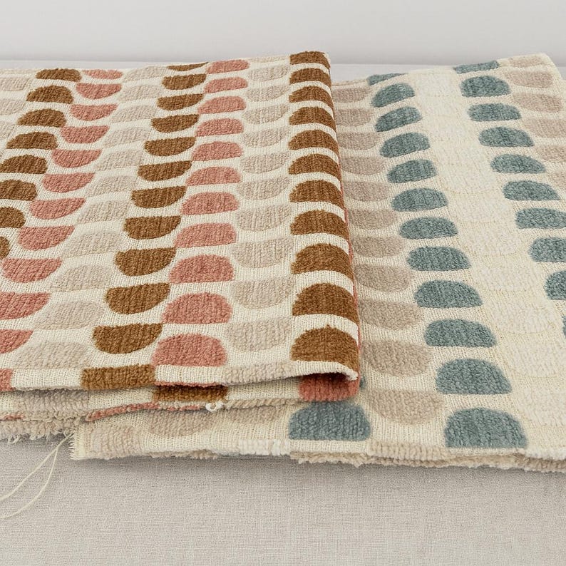 May include: Two rolls of patterned fabric. One has rows of half-circle shapes in brown, pink, and beige on a cream background. The other has blue-green half-circles on a cream background. The fabrics have a textured finish.