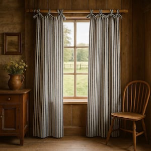 May include: Striped blue and cream curtains hang in a wooden-paneled room, framing a window with a view of a green field. The curtains are tied back with matching fabric. A wooden chair and cabinet complete the rustic scene.