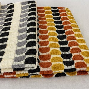 May include: Two folded textured fabric pieces with repeating patterns. One has vertical rows of black, grey, and white leaf shapes. The other has rows of orange, black, and yellow half-circle shapes. The fabrics appear to be towels or upholstery.