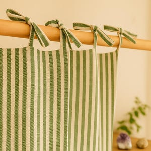 May include: Green and white striped curtains hanging from a wooden rod. The curtains are made of a textured fabric and are tied with matching green and white striped bows. The overall theme is home decor.