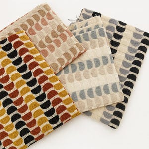 May include: Several fabric swatches with a repeating half-circle pattern. The colours include brown, black, yellow, grey, and beige. The fabrics are arranged on a white surface. Measurements are not available.