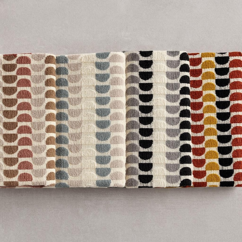 May include: Folded towels with a repeating semi-circle pattern in various colours. The towels feature brown, beige, grey, black, red, and yellow. The design is geometric and modern, suitable for a bathroom.