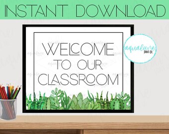 May include: A printable classroom sign with a white background and black text that reads "Welcome to our classroom". The sign is framed with a black border and features a green watercolor illustration of succulents at the bottom.