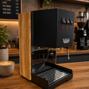 Peut inclure: Une machine à expresso Gaggia Classic avec une finition noir mat et des panneaux latéraux en bois clair. La façade comprend trois interrupteurs à bascule noirs, trois voyants rouges, un bac d'égouttage en métal et une buse vapeur argentée.