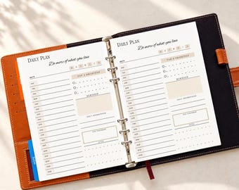 May include: A brown leather binder with a six-ring metal mechanism holding white daily planner pages. The pages feature the text Daily Plan and Do more of what you love, with sections for date, top 3 priorities, reminders, and hourly schedules.