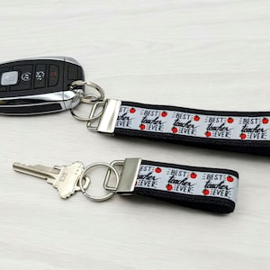 May include: Black and white key chain with a silver key ring and a black ribbon with the text "Best Teacher Ever" repeated. The ribbon has red apple icons.