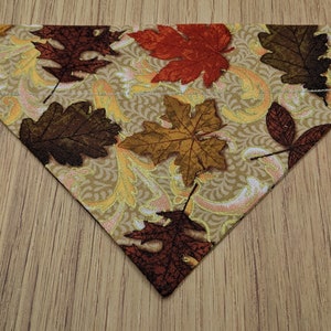 Puede incluir: Un bandana para perro de color marrón, dorado y rojo con un diseño de hojas de otoño.
