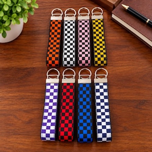 May include: Eight fabric wristlet keychains arranged in two rows, each featuring a checkered pattern in orange, black and white, pink, yellow, purple, red, blue, or navy blue, finished with a silver-toned metal clasp and a split ring.
