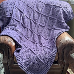 May include: A purple crocheted throw blanket with a repeating circular pattern, draped over a brown leather armchair.