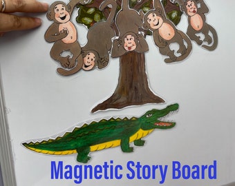 Könnte beinhalten: Magnettafel mit einem Baum, Zeichentrickaffen, einem grünen und gelben Krokodil und Zahlenkarten von 0 bis 5. Der Text "Magnetic Story Board" wird unten angezeigt.