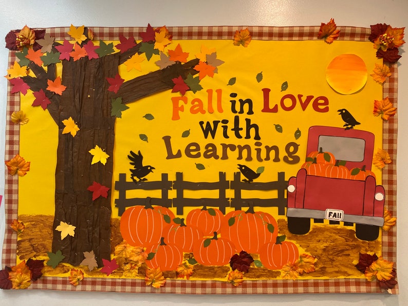 K&ouml;nnte beinhalten: Ein gelbes Bulletin Board mit Herbstthema. Das Board zeigt einen braunen Baum mit roten, orangen und gelben Bl&auml;ttern. Der Text "Fall in Love with Learning" ist in roten, orangen und gelben Buchstaben geschrieben. Ein roter LKW mit einem wei&szlig;en "FALL" -Kennzeichen transportiert K&uuml;rbisse. Der LKW steht vor einem braunen Zaun.