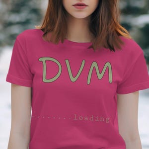 Puede incluir: Una camiseta rosa con el texto "DVM...loading" en verde.