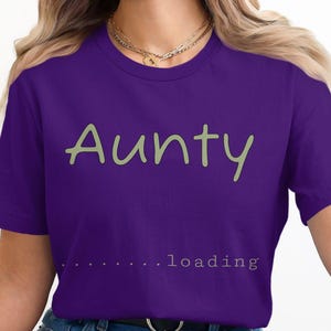 May include: Purple t-shirt with the text "Aunty...loading" in a light green colour.