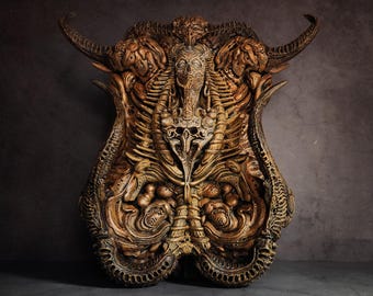 May include: A detailed, brown-toned sculpture with a complex, organic design. The artwork features a central skeletal structure, curved horns, and intricate, textured surfaces. The piece has a dark, weathered appearance, suggesting an aged or antique aesthetic.