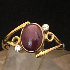 May include: A gold ring with a large oval-shaped purple gemstone and two smaller clear gemstones on the band.
