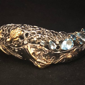 Può includere: Un braccialetto in argento e oro con un design dettagliato che presenta una tartaruga e pietre di topazio blu.