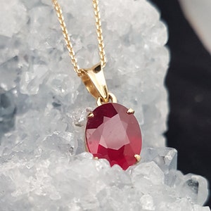 May include: A gold chain necklace with a pendant featuring a large, oval-shaped ruby gemstone.
