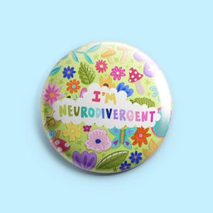Puede incluir: Un botón redondo con fondo verde claro, con flores, setas y mariposas coloridas. El texto "I'M NEURODIVERGENT" se muestra en una burbuja de texto blanca con forma de nube. El botón tiene un acabado brillante.