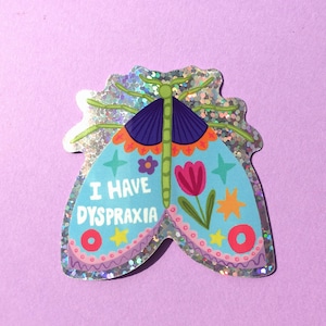 May include: A sticker featuring a colorful moth design with the text "I HAVE DYSPRAXIA." The moth has blue wings with floral and star accents, a purple head, and a green body. The sticker has a glittery, iridescent border.