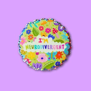 May include: A circular pin with a scalloped edge, displaying the text "I'M NEURODIVERGENT". The design features a green backdrop with flowers, mushrooms, and leaves. The text is in rainbow hues, and the edge has a glittery, iridescent finish.