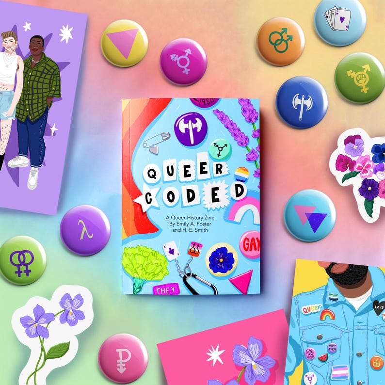 K&ouml;nnte beinhalten: Ein blaues und rosa Zine mit dem Titel "Queer Coded: A Queer History Zine by Emily A. Foster and H. E. Smith". Das Zine ist von bunten Kn&ouml;pfen und Aufklebern mit LGBTQ+-Symbolen umgeben.