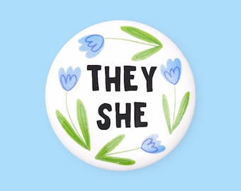 Könnte beinhalten: Weißer Knopf mit blauen Blumen und grünen Blättern um den Text "THEY SHE" in Schwarz.