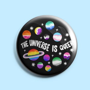May include: A circular black badge with the white text "THE UNIVERSE IS QUEER". The design includes colourful planets and stars. A rainbow planet with a ring is also featured. The badge has a space or galaxy theme.