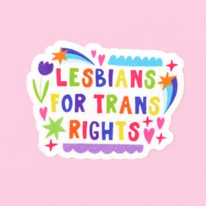 Può includere: Un adesivo bianco con il testo "Lesbiche per i diritti trans" in colori arcobaleno. L'adesivo è decorato con cuori, stelle e altri disegni colorati.