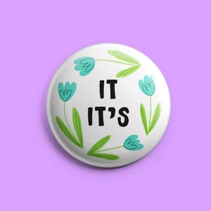 以下が含まれることがあります： 「IT IT'S」の黒い文字が書かれた白いボタン。 ターコイズブルーの花のイラストと緑の茎と葉で囲まれています。 ボタンはラベンダー色の背景に配置されています。