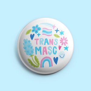 May include: A white button with the words "TRANS MASC" in pink and blue, surrounded by floral and rainbow graphics. The button also features a smiley face, hearts, and stars.