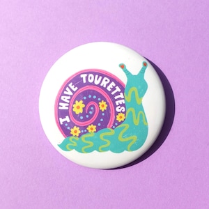 Puede incluir: Un botón blanco con un diseño de caracol de dibujos animados. El caracol es de color turquesa y amarillo con las palabras "I HAVE TOURETTES" en espiral alrededor de su caparazón. El fondo es de color púrpura liso.