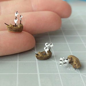 Puede incluir: Primer plano de pequeños botes artesanales con cascos marrones y velas blancas. Los pequeños veleros están dispuestos sobre una superficie gris. Los botes tienen dos o tres velas cada uno, con un tema náutico.