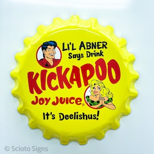 May include: Yellow metal bottle cap shaped sign with a red and white illustration of a cartoon man and woman. The sign reads "Lil' Abner Says Drink Kickapoo Joy Juice. It's Deelishus!"