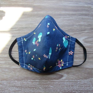 May include: A blue face mask with a white stitched border and a pattern of colorful mushrooms and flowers.