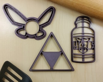 Puede incluir: Tres cortadores de galletas de plástico morado con forma de personaje de videojuego, triángulo y cartón de leche con una vaca.