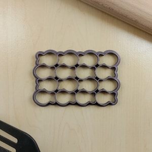 May include: A gray plastic cookie cutter with 16 individual cutouts shaped like fish. The cutter is on a light wood surface.
