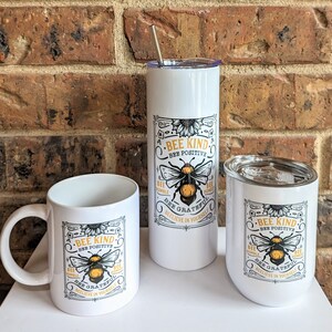 May include: Three white ceramic mugs with a bee graphic and the text "Bee Kind, Bee Positive, Bee Grateful, Believe in Yourself". The mugs are in different sizes, with the largest mug being a tumbler with a straw.