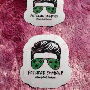 May include: Two white stickers with a cartoon illustration of a person wearing sunglasses with marijuana leaf designs. The text on the stickers reads "Pothead Summer" and "@marijumelli Designs".