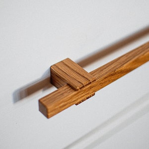 May include: A wooden cabinet door handle with a rectangular shape and a natural wood finish.