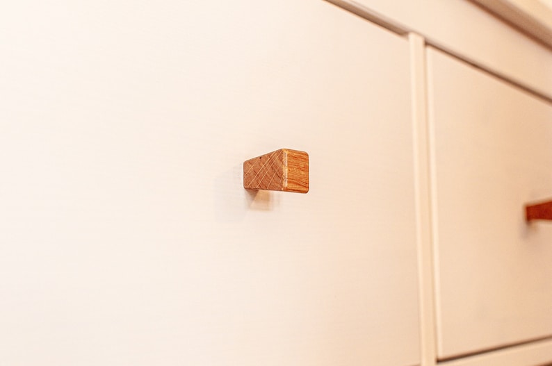May include: Close-up of a white dresser drawer with a wooden knob. The knob is square and has a light brown finish.