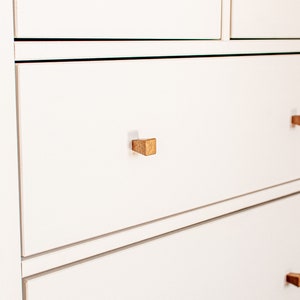 May include: White chest of drawers with six drawers and wooden knobs. The drawers have a subtle lip around the edge.