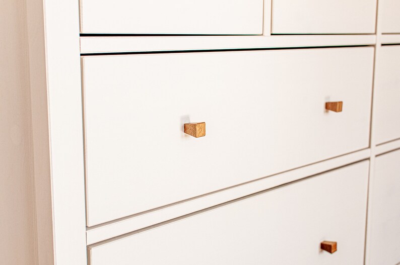 May include: White chest of drawers with six drawers and wooden knobs. The drawers have a subtle lip around the edge.