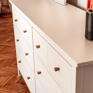 May include: White chest of drawers with six drawers and wooden knobs. The dresser has a white top and is made of wood.