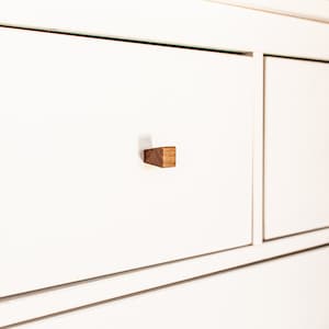 May include: White dresser with three drawers and wooden knobs. The drawers have a subtle lip around the edges.