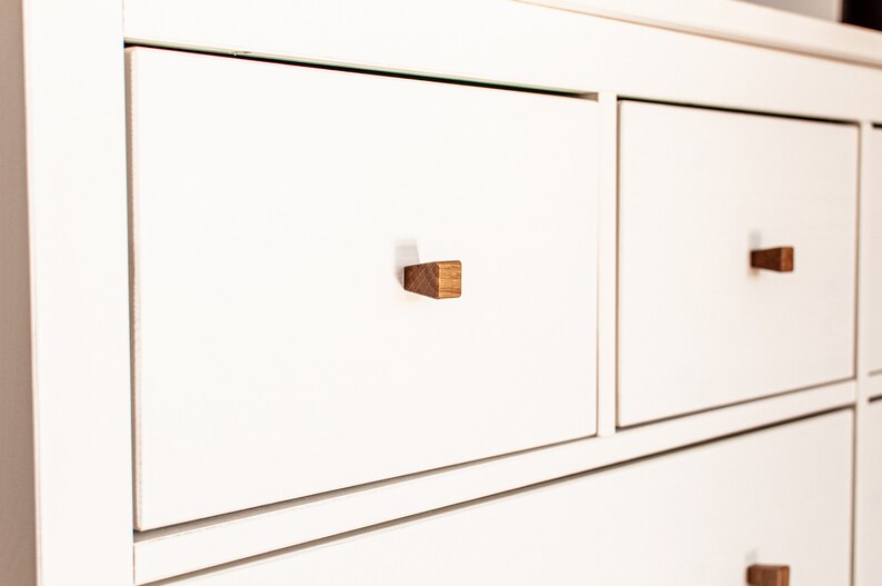 May include: White dresser with three drawers and wooden knobs. The drawers have a subtle lip around the edges.