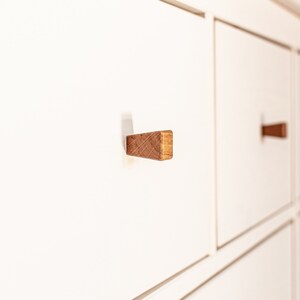 May include: White chest of drawers with six drawers and wooden knobs. The drawers have a subtle lip around the edges.