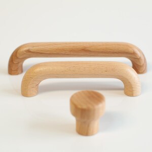 May include: Three wooden cabinet knobs in various sizes. The knobs are made of light brown wood and have a smooth, rounded finish.